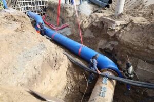 Свързване на магистрален водопровод с син фасонен детайл в дълбок изкоп за държавна ВиК инфраструктура.