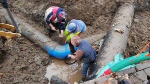 Аварийна ремонтна връзка с син фасонен елемент върху магистрален водопровод в кални условия.