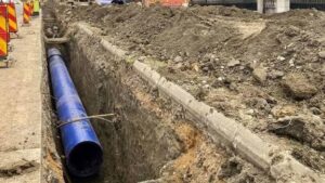 Подмяна на уличен водопровод със синя тръба в тесен изкоп по градска улица.